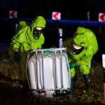 Chemical spill container with two men in HAZMAT suits moving it